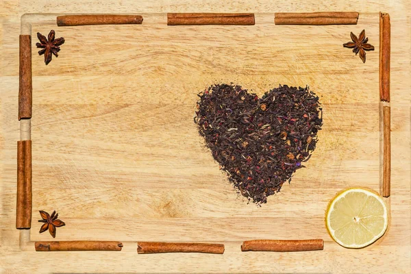 Baharatlı kırmızı çaydan yapılmış bir kalp: anason, tarçın ve ahşap kesme tahtasındaki bir limon dilimi, üst manzara. Yemek ve yemek konsepti.