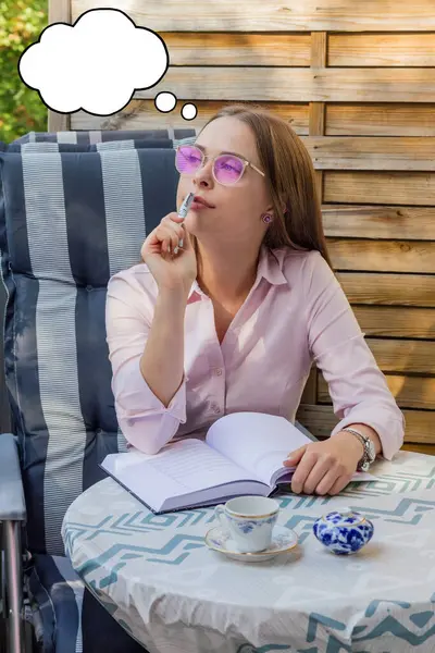 Pembe gözlüklü genç ve tatlı bir kızın kafasının üstünde düşünce baloncuklarıyla notlar alırken düşünmesi. Dünyaya gül renkli gözlüklerle bakmak. Düşünme baloncuğu ile görüntü. Balkonda. Öğrenme kavramı.