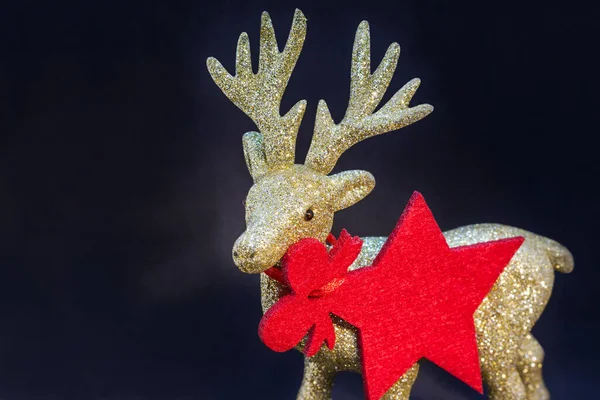 Koyu bir arka planda altın, parlak ren geyiği heykelciği. Noel arkaplanı / kartı, hediye kartı, kırmızı yıldız - kolye / etiket. Kopya alanı olan Noel duvar kâğıdı.