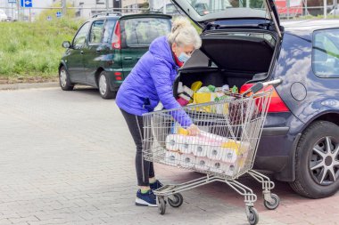 Koruyucu maske takan son sınıf güzel bir kadın otoparktaki bir arabaya alışveriş yapıyor. Koronavirüs salgını sırasında günlük yaşam.