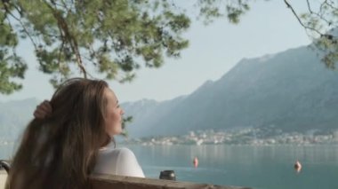Genç bir kadın, sakin bir Kotor Körfezi 'nin arka planında dağlarla dinlenerek huzurlu bir anın tadını çıkarıyor. Yüksek kalite 4k görüntü