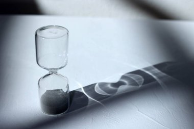 Masanın üzerindeki kum saati ışık, gölge ve cam yansımaları vuruyor.