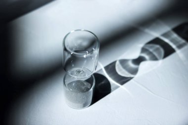 Masanın üzerindeki kum saati ışık, gölge ve cam yansımaları vuruyor.