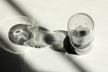 Masanın üzerindeki kum saati ışık, gölge ve cam yansımaları vuruyor.