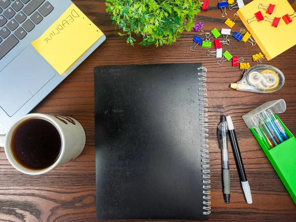 Flat lay, black book mock up. workspace in the background of the office desk from the top view. A workspace with black books, laptops, office supplies, pencils, green leaves, and coffee cups against the backdrop of a wooden table.