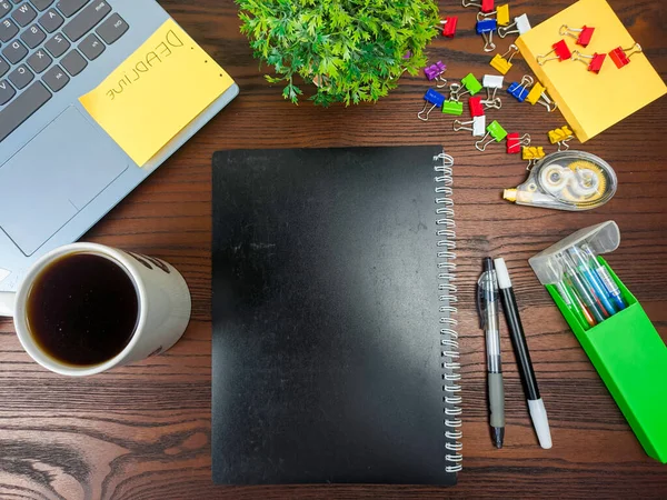 Flat lay, black book mock up. workspace in the background of the office desk from the top view. A workspace with black books, laptops, office supplies, pencils, green leaves, and coffee cups against the backdrop of a wooden table.