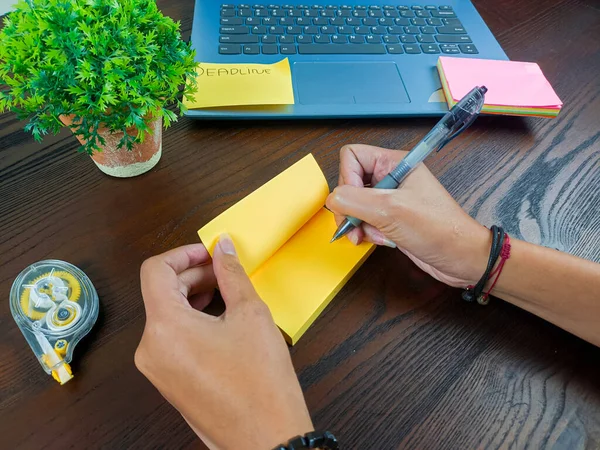 women write in yellow notes, mock up yellow notes. Women\'s hands write notes on yellow note paper in the background of the office desk workspace from the top view.