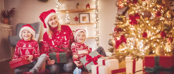 stock image Mother and her son ad daughter sitting indoors with Christmas present boxes in their hands. Concept of celebrating of Christmastime and New Year together.