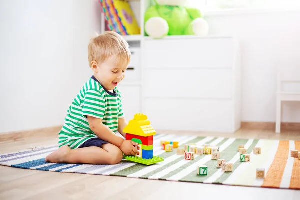 Cute boy sitting on the carpet indoor and playing with plastic constructor. Concept of the childhood and family.