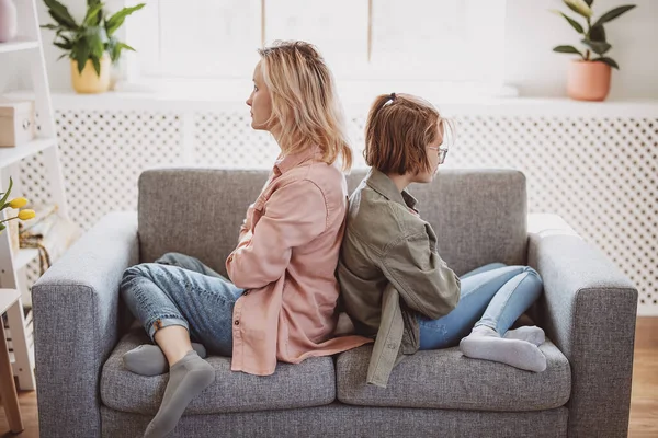 Quarreled mother and daughter sitting on the sofa back to back. Concept of the family relation.