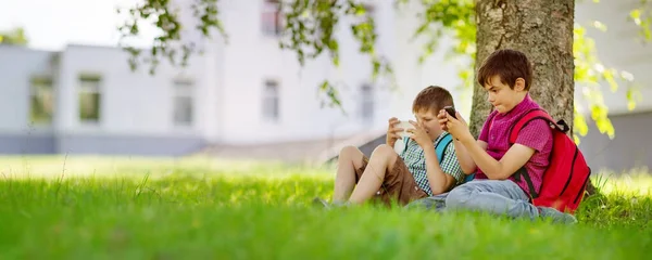 Dois Rapazes Com Smartphones Nas Mãos Sentados Relva Perto Escola — Fotografia de Stock