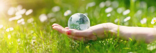 Woman hands holding a glass sphere of Earth on the green grass background. Concept of saving planet and our future.