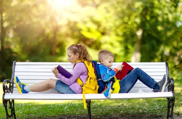 男孩和女孩一起坐在教育大楼附近的长椅上 回到学校的概念 图库图片