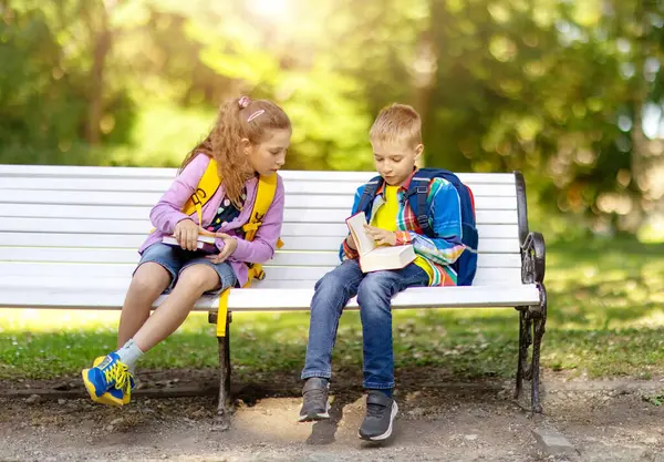 男孩和女孩一起坐在教育大楼附近的长椅上 回到学校的概念 免版税图库照片