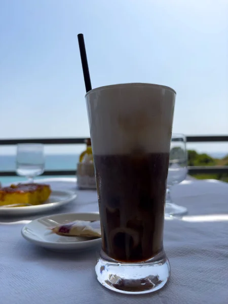 Bir bardak buzlu kahve, arka planda turuncu kek olan bir masanın üstünde. Yüksek