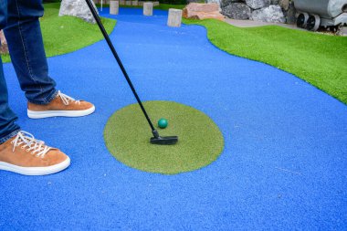 MInigolf player with brown sneakers putting golf ball into the hole. High quality photo clipart