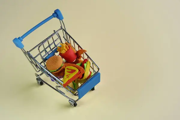 Closeup image of shopping cart full with junk foods like burger, fries and pizza. Copy space for text. Bad eating habits concept.