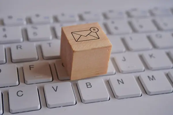 Wooden cube with new email notification icon on top of keyboard. Communication and technology concept