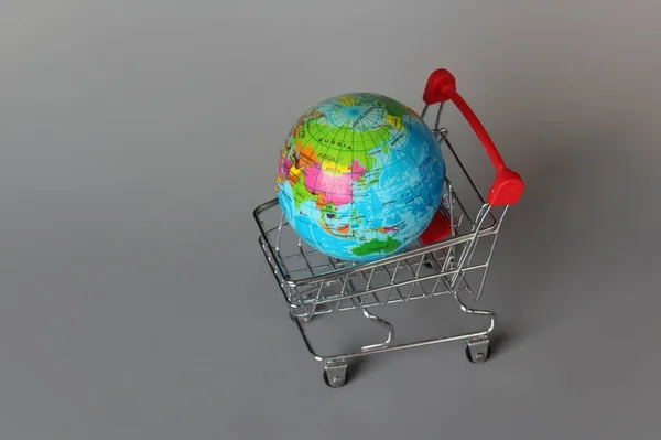 Global market, international market concept. Mini shopping trolley and globe on grey background