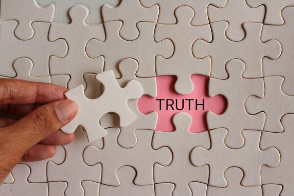 Closeup image of hand pickup puzzle and reveal the word TRUTH. 