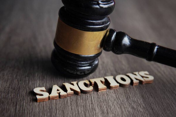 Close up image of judge gavel and text SANCTIONS on wooden table.