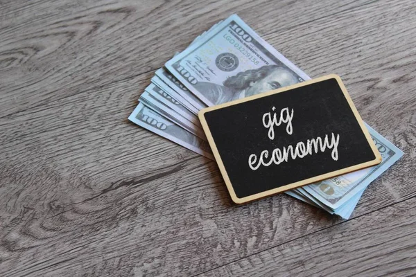 Chalkboard with text GIG ECONOMY on top of money with copy space. Business and finance concept.