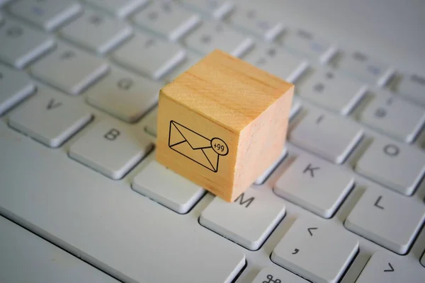 Wooden cube with new email notification icon on top of keyboard. Communication and technology concept