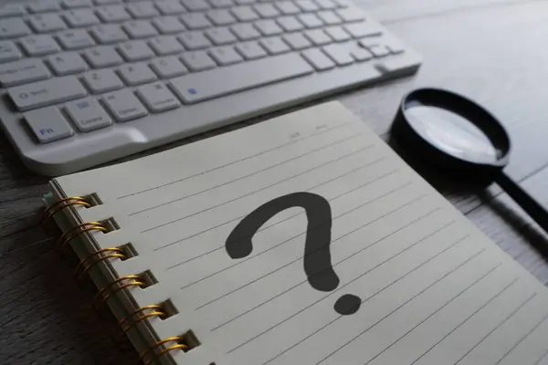 Closeup image of notebook with question mark, magnifying glass and keyboard.