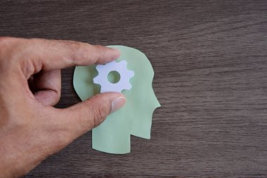 Kafasının ortasında beyaz bir dişli olan insan kafasından kesilmiş yeşil bir kağıt parçası. Uzayı metin için kopyala. Beyin fırtınası, düşünme konsepti.