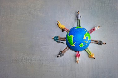 Çeşitli renklerde minyatür oyuncak insanlardan oluşan bir grup gri bir yüzey üzerinde bir dünyanın etrafında dikiliyorlar. Uzayı metin için kopyala. Dünya günü, çeşitlilik ve çok ırklı kavram.