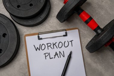 Üzerinde çalışma planı olan bir panonun, siyah bir dambıl ve ağırlık plakasının yanına yakın plan resmi. Spor ve spor konsepti.
