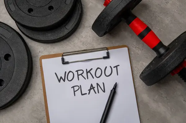 Üzerinde çalışma planı olan bir panonun, siyah bir dambıl ve ağırlık plakasının yanına yakın plan resmi. Spor ve spor konsepti.