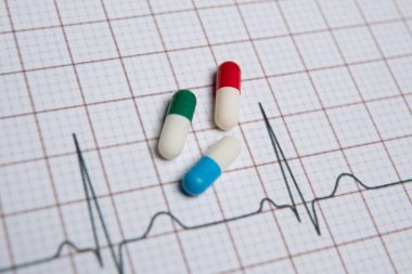 Elektrokardiyogramda (ECG) farklı renklerde üç hapın yakın çekimi. Kalp hastalığı ve ilaç konsepti.