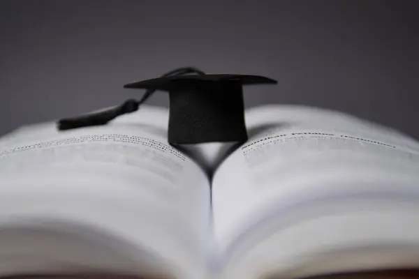 stock image A black graduation cap on an open book. Education, knowledge concept.