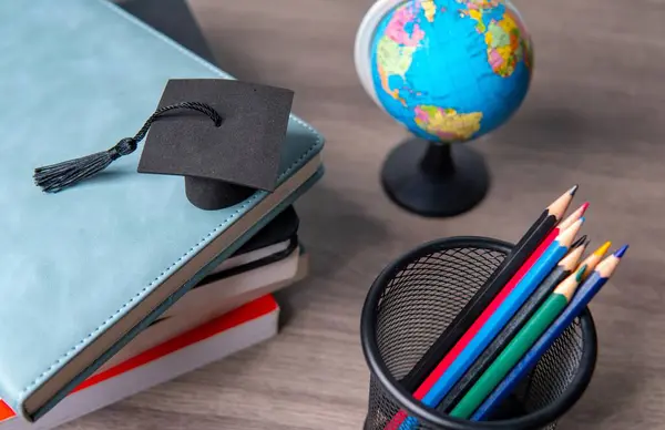 Mezuniyet şapkası, bir yığın kitap, bir küre ve renkli kalem koleksiyonu. Eğitim ve öğrenme kavramı.