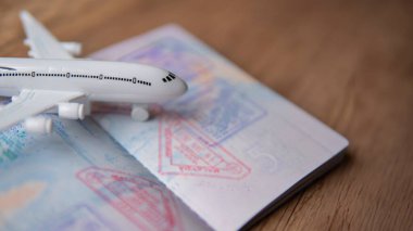 Açık bir pasaportun üstüne çeşitli pullarla yerleştirilmiş beyaz bir uçağın yakın çekimi. Turizm, küresel seyahat, havacılık endüstrisi ve uluslararası seyahat kavramı.