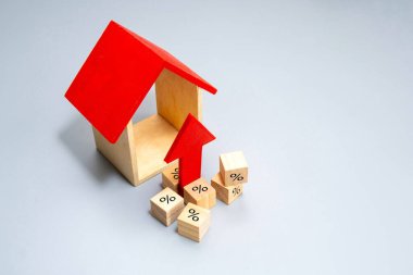 A house model with a upward pointing red arrow and blocks displaying percentage symbols. Rising housing costs, increasing interest rates concept.