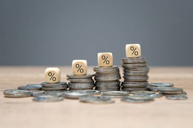 Her biri artan faiz oranlarını veya finansal büyümeyi temsil eden madeni para yığınının üstüne yerleştirilmiş yüzdelik sembollü tahta bloklar..