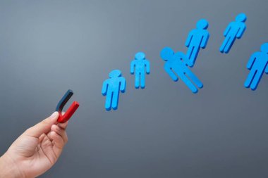 Mıknatıs tutan bir el mavi ahşap figürleri çeker. Çekim konsepti.
