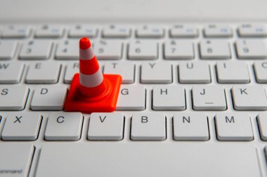 A miniature traffic cone placed on a computer keyboard. Website maintenance, technical difficulties, website under construction concept. clipart