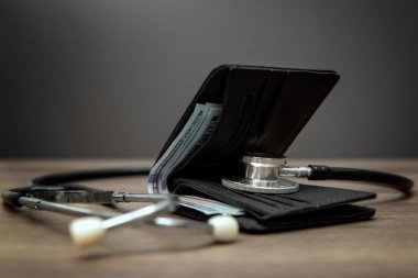 Bir steteskop açık bir cüzdanın yanındaki ahşap bir masada yatıyor ve para dökülüyor. Sağlık hizmetleri kavramının maliyeti.