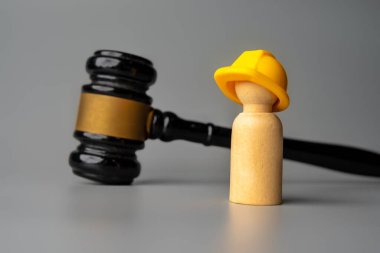 Sert şapka takan tahta bir bebek tokmağın önünde duruyor. İnşaat hukuku, işçi güvenliği veya inşaat endüstrisi kavramındaki hukuki anlaşmazlıklar.