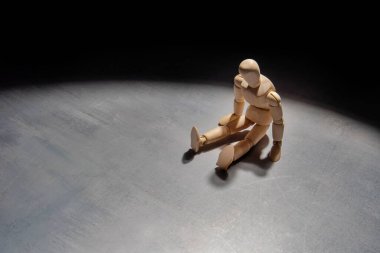 Tahta bir manken karanlıkta tek başına oturur, yalnızlığı, yalnızlığı ve umutsuzluğu simgeler..