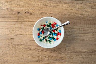 Renkli kapsüller ve kaşıkla dolu beyaz bir kase. Tıbbi ve sağlık hizmeti kavramı.