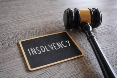 Bir yargıç tokmağı ve içinde INSOLVENCY yazan bir karatahta. Yasal işlemler, mali düzenlemeler ve iflas kavramı.