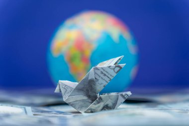 Bir origami kuşu bir Amerikan doları ve bir küreden katlandı. Uluslararası para transferleri, havaleler ve küresel para hareketi kavramı.