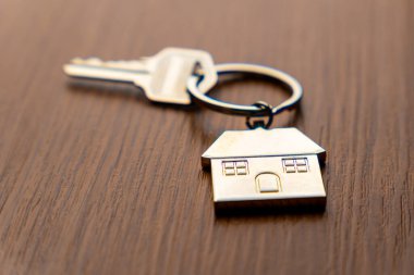 Masanın üzerindeki metal ev şeklindeki anahtarlığa bağlı bir anahtar. Ev sahipliği, gayrimenkul, mülk ve yeni başlangıç kavramı.