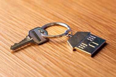 Masanın üzerindeki metal ev şeklindeki anahtarlığa bağlı bir anahtar. Ev sahipliği, gayrimenkul, mülk ve yeni başlangıç kavramı.