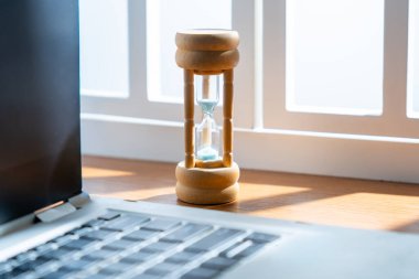 Dizüstü bilgisayarın yanında küçük bir kum saatinin yakın çekimi. Verimlilik, son teslim tarihi, zaman yönetimi kavramı.