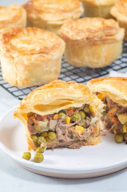 Sliced beef pot pie on plate, pies on a cooling rack, vertical